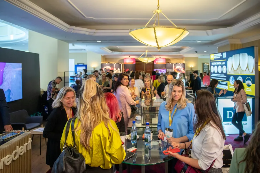 Expoziția congresului: medici în fața standurilor, sub un candelabru.