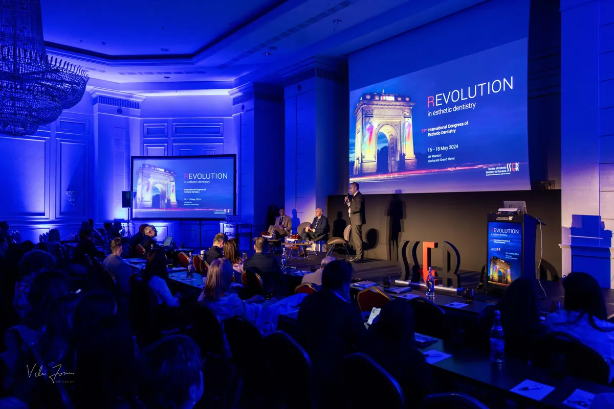 Sala congresului în lumină albastră, cu scena și ecranele ediției a 21-a, „Revolution in esthetic dentistry”, 2024.